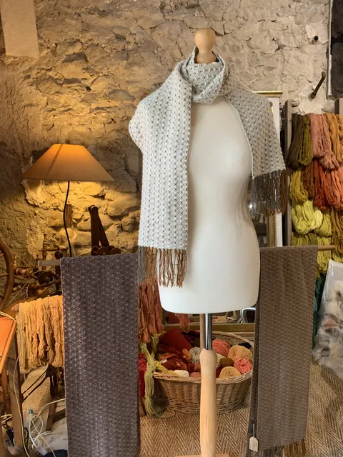 Écharpes tissées main dans l'atelier : une écrue à motifs sur un buste, deux brunes à côté