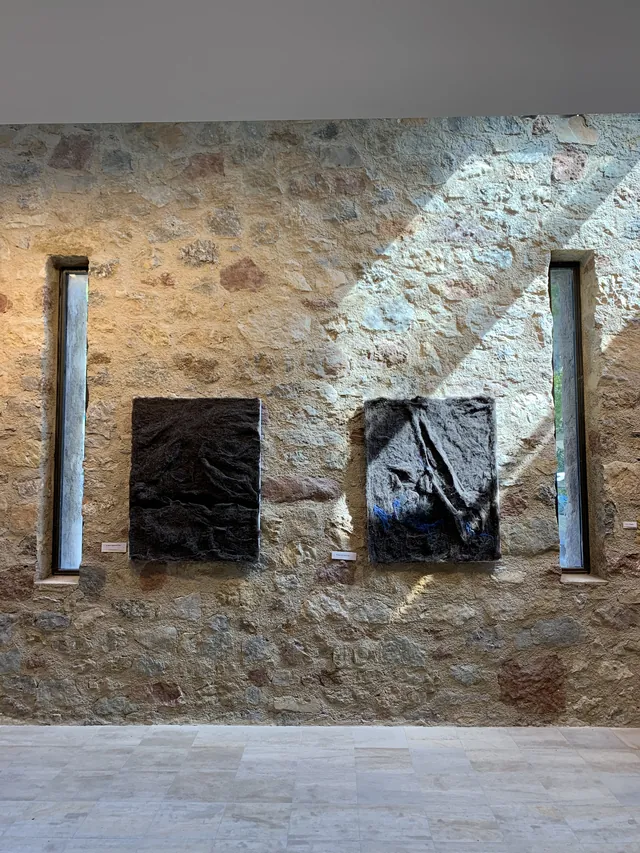 Deux tentures noires texturées exposées sur un mur de pierre