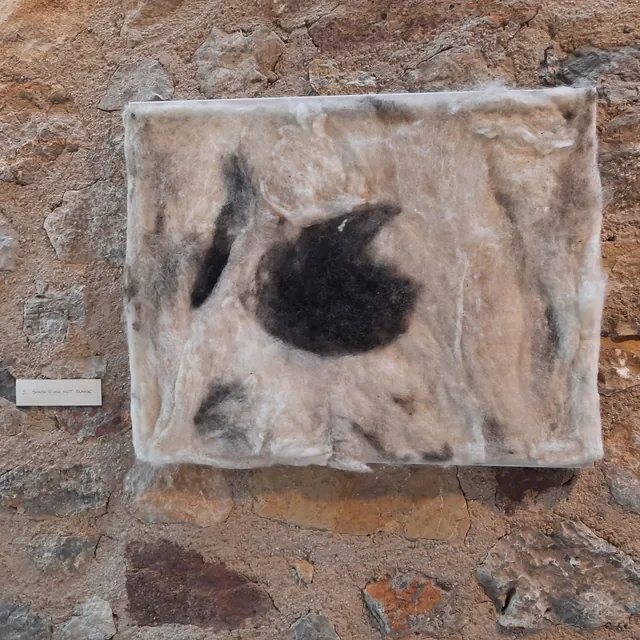 Œuvre en laine feutrée écrue et noire, sur un mur de pierre