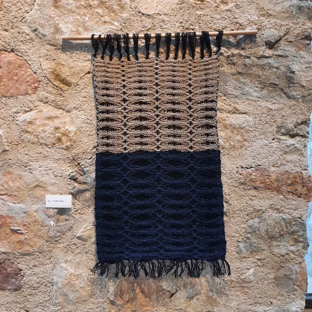 Tenture tissée main bleu nuit et écrue, frangée, sur un mur de pierre